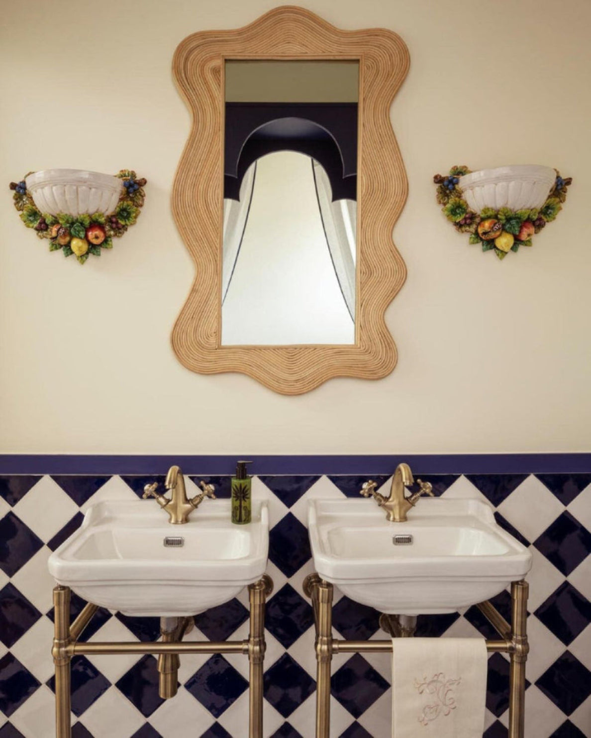 Bathroom with two sinks, rattan decorative mirror heaps and woods, and wall sconces on a white and blue tiled wall.